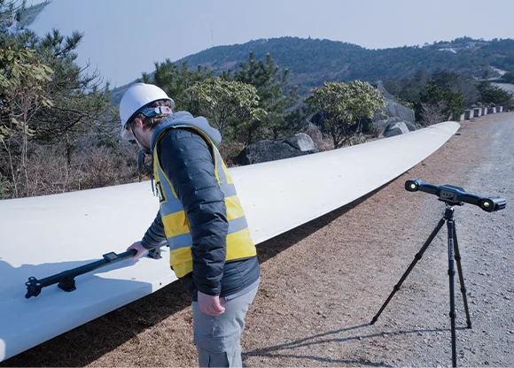 FreeScan UE Nova Series | Video Photogrammetry (VPG) Technician using a calibration rod beside a large industrial blade with tripod-mounted equipment, illustrating the FreeScan UE Nova Series video photogrammetry workflow.