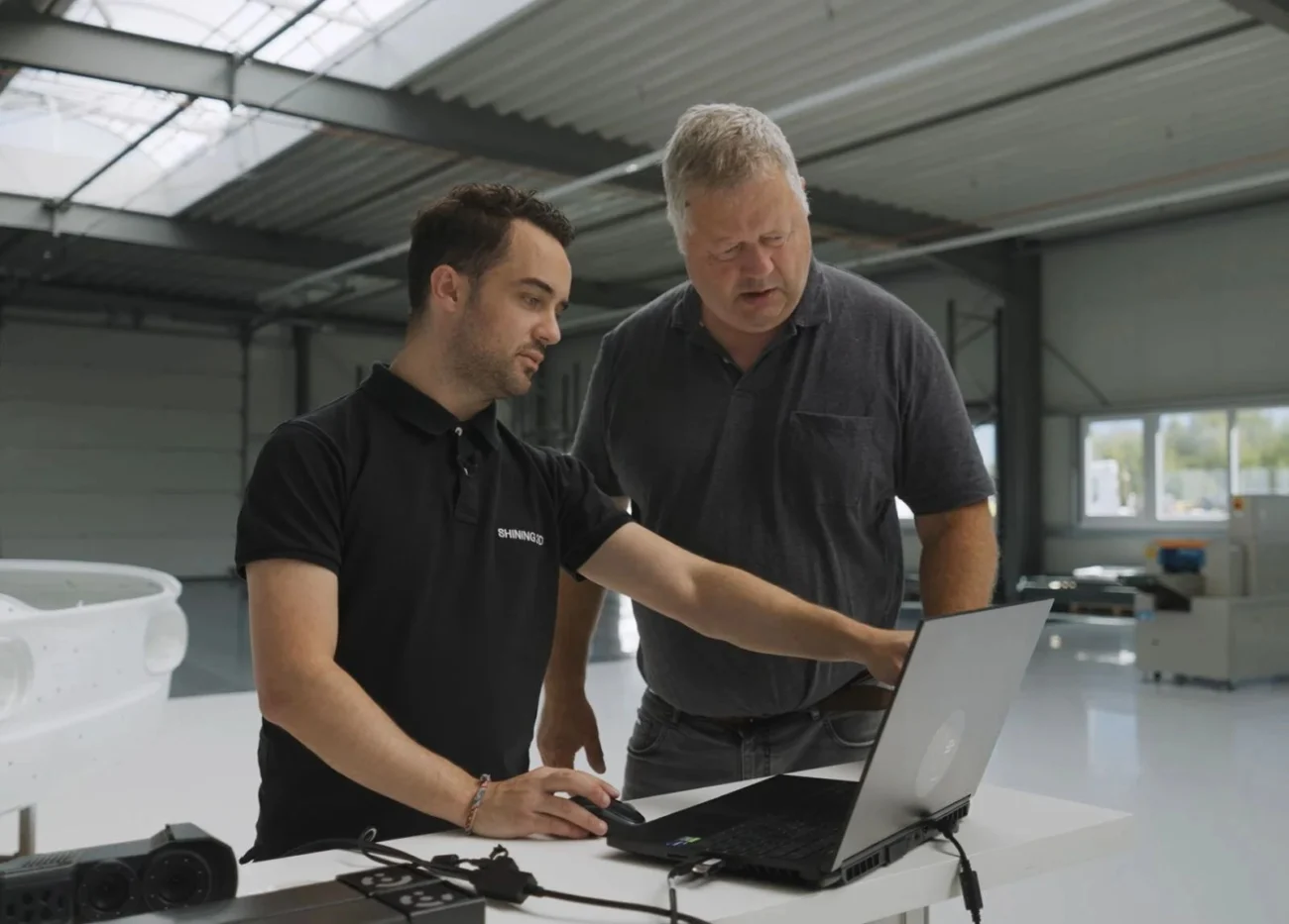 SHINING 3D Technical Support and Application Guidance SHINING 3D specialist assisting a customer with technical software guidance on a laptop in an industrial workshop.